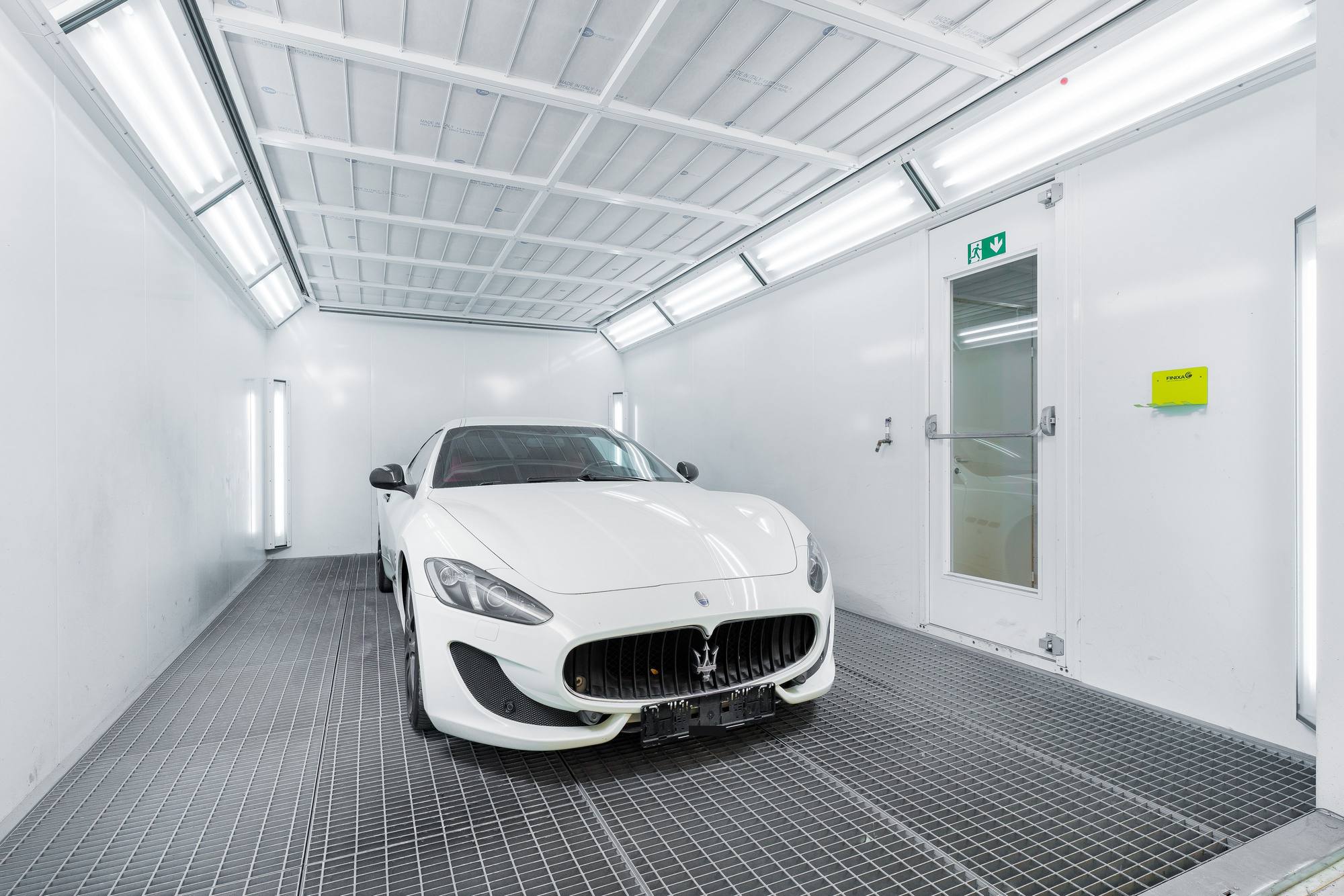 A white car inside a brightly lit vehicle paint spray booth